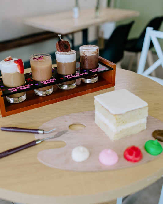 ✨ Valentine’s Cake Decorating Event – Feb 13th | 4:00pm–6:30pm ✨ - Rising For People Coffee Co.Rising For People Coffee Co.Rising For People Coffee Co.cake decorating and coffee flights for valentines day and cake on a table with a paint palette and brush.